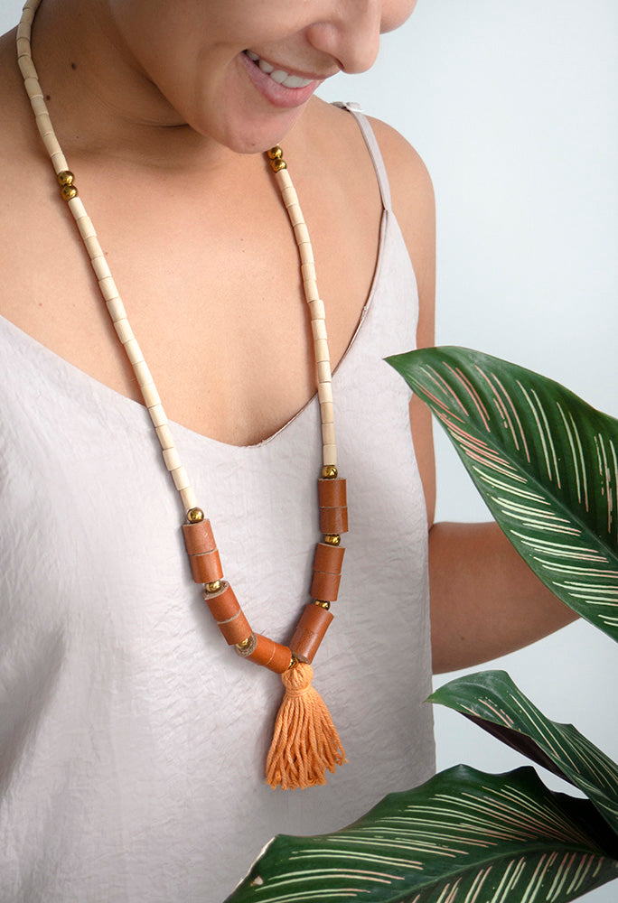 Mujer sonriente con blusa beige de tirantes usando el collar BOHO en el cuello, en colores miel y naranja