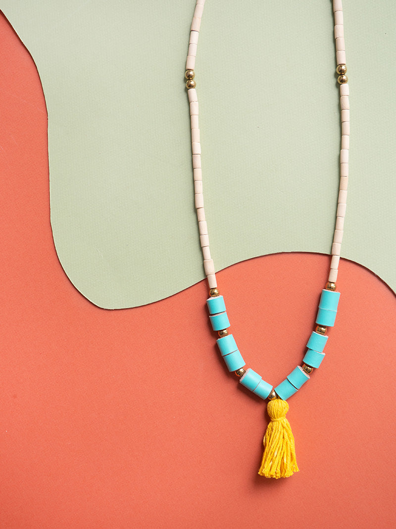 Collar largo de piezas de madera natural con rollitos en cuero color turquesa, bolitas doradas de acero inoxidable y rollito de hilos de algodón en amarillo teñidos con tintes naturales de curcuma.