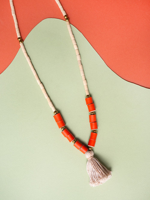 Collar largo de piezas de madera natural con rollitos en cuero color naranja, bolitas doradas de acero inoxidable y rollito de hilos de algodón en gris teñidos con tintes naturales de frijoles negros.