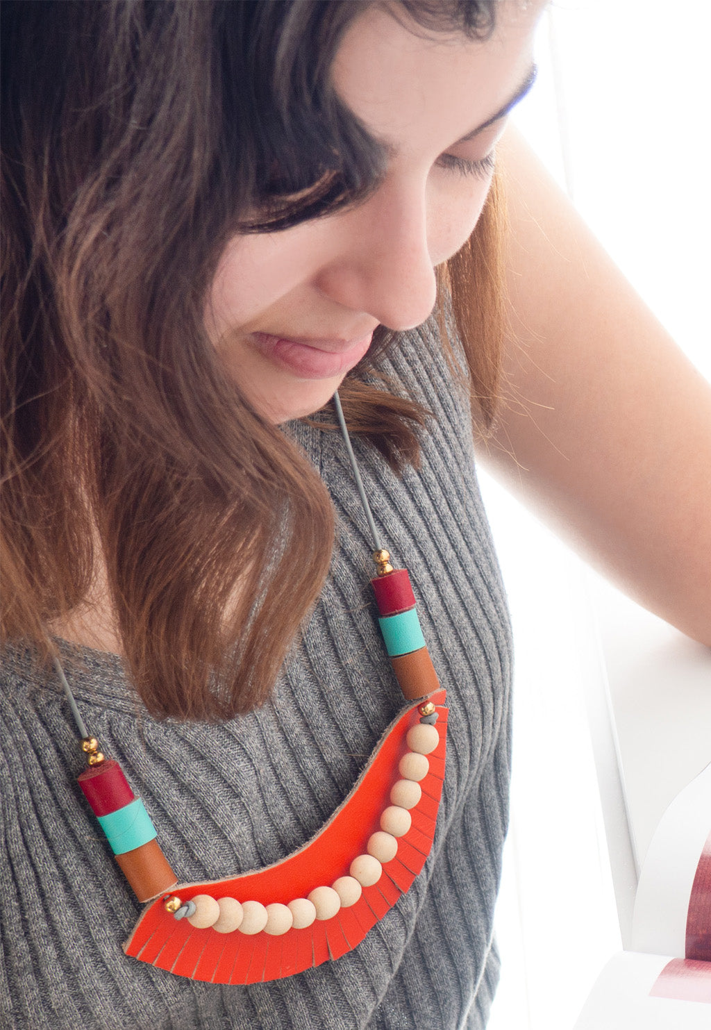 Mujer usando el collar Cleo naranja sobre una blusa de color gris leyendo una revista