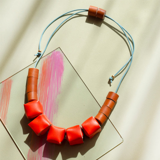 Collar ajustable hecho de retazos de cuero, cubos de color naranja y rollitos color miel con cordón en cuero celeste