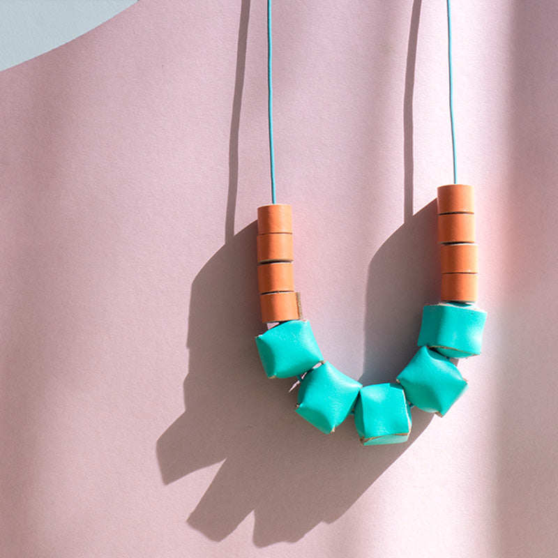 Collar ajustable hecho de retazos de cuero, cubos de color turquesa y rollitos color durazno con cordón en cuero celeste