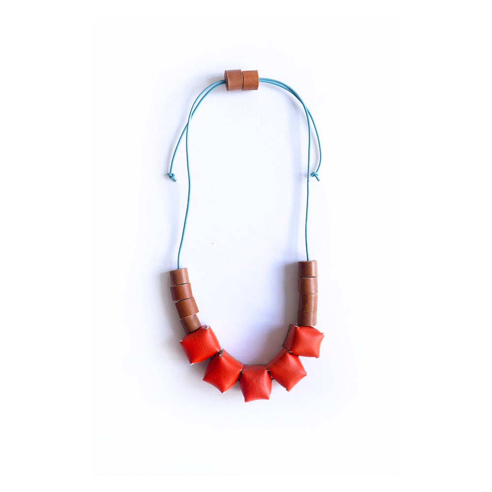 Collar ajustable hecho de retazos de cuero, cubos de color naranja y rollitos color miel con cordón en cuero celeste