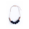Collar ajustable hecho de retazos de cuero, cubos de color negro y rollitos color salmón con cordón en cuero café