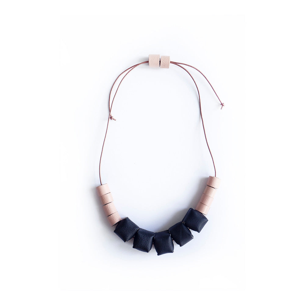 Collar ajustable hecho de retazos de cuero, cubos de color negro y rollitos color salmón con cordón en cuero café