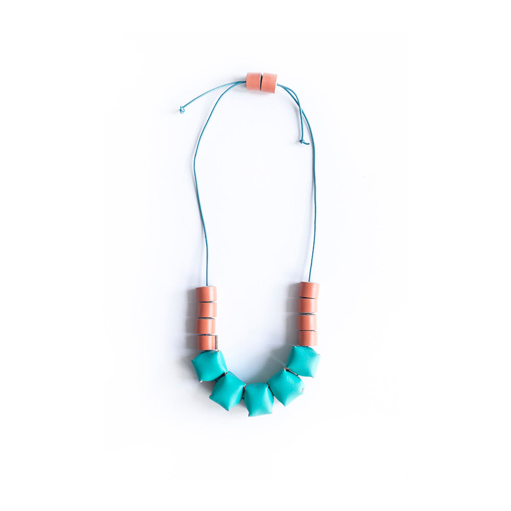 Collar ajustable hecho de retazos de cuero, cubos de color turquesa y rollitos color durazno con cordón en cuero celeste