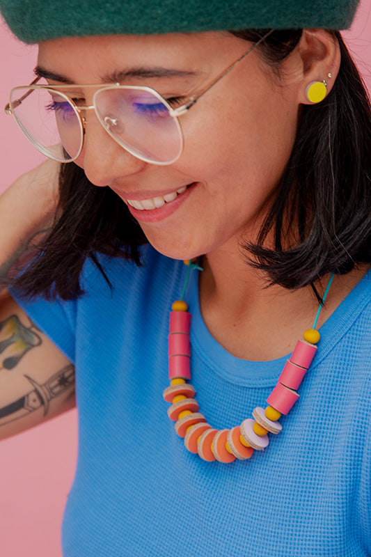 Mujer con blusa azul usando el collar Maca de cuero en color fucsia y amarillo