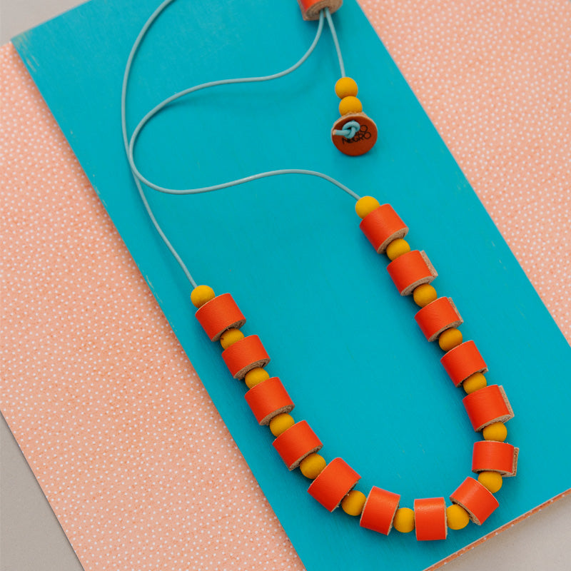 Collar completo hecho con rollitos de cuero color naranja con bolitas de madera amarillas teñidas con tinte natural extraído de la cúrcuma, cierre ajustable, cordón de cuero celeste