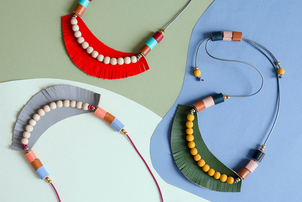 Detalle desde arriba de las tres opciones de color del collar sobre fondo azul, verde olivo y verde claro. Se ven el collar naranja, gris y verde juntos