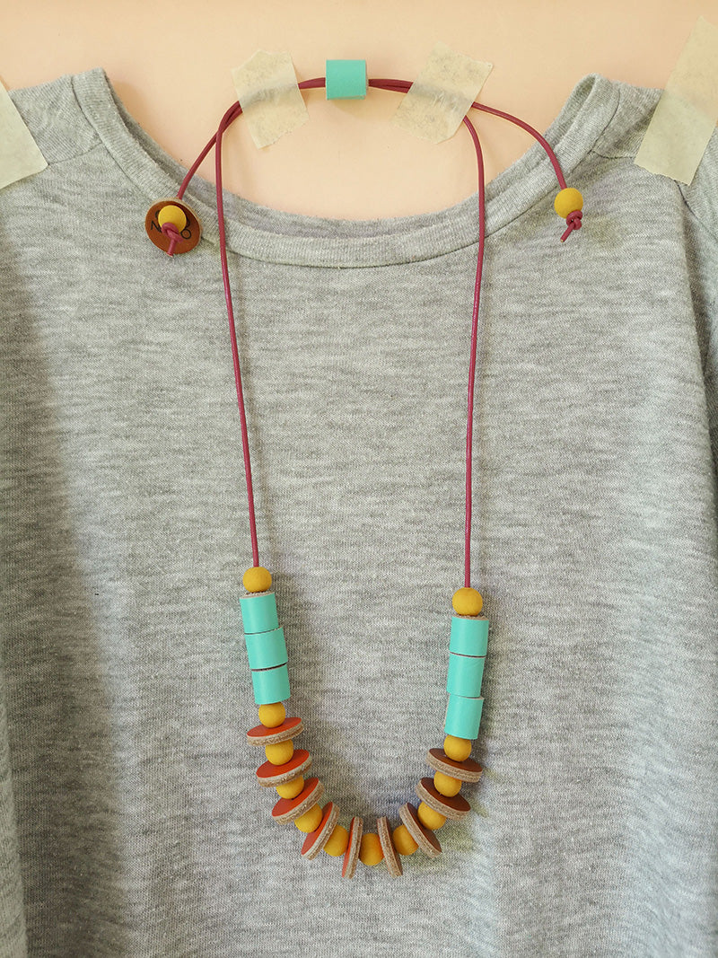 Collar Maca, madera y cuero turquesa sobre abrigo gris