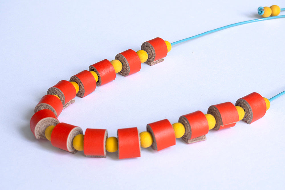 Detalle de rollitos de cuero naranja y bolitas de madera amarillas