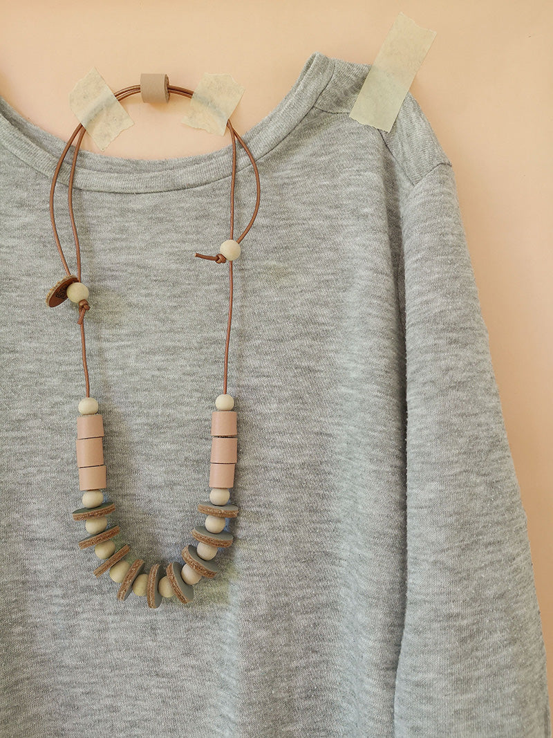 Collar Maca, madera y cuero salmón sobre abrigo gris