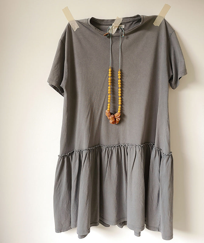 Collar Nudos de cuero miel y bolitas madera amarillo sobre vestido gris