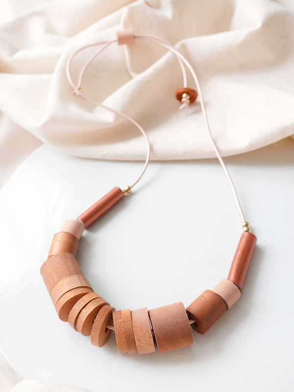 Detalle de collar Origen, piezas de madera cilíndricas y tubos de cuero color cobre y salmón