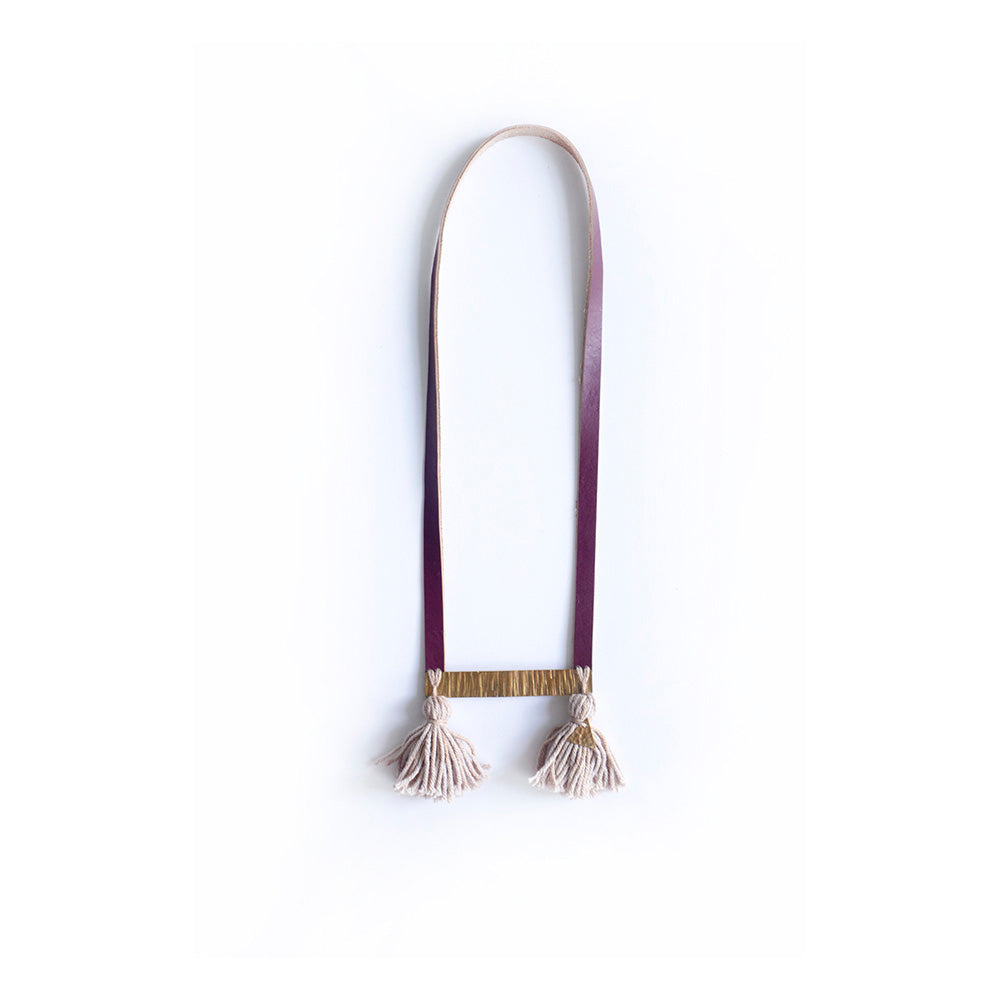 Collar Sara, tira de cuero vino cosida a pieza rectangular de bronce, a ella están cosidos en cada extremo un rollito de hilos de algodón color gris teñido con tinte natural de frijoles negros y un rollito tiene cosido un triángulo de bronce