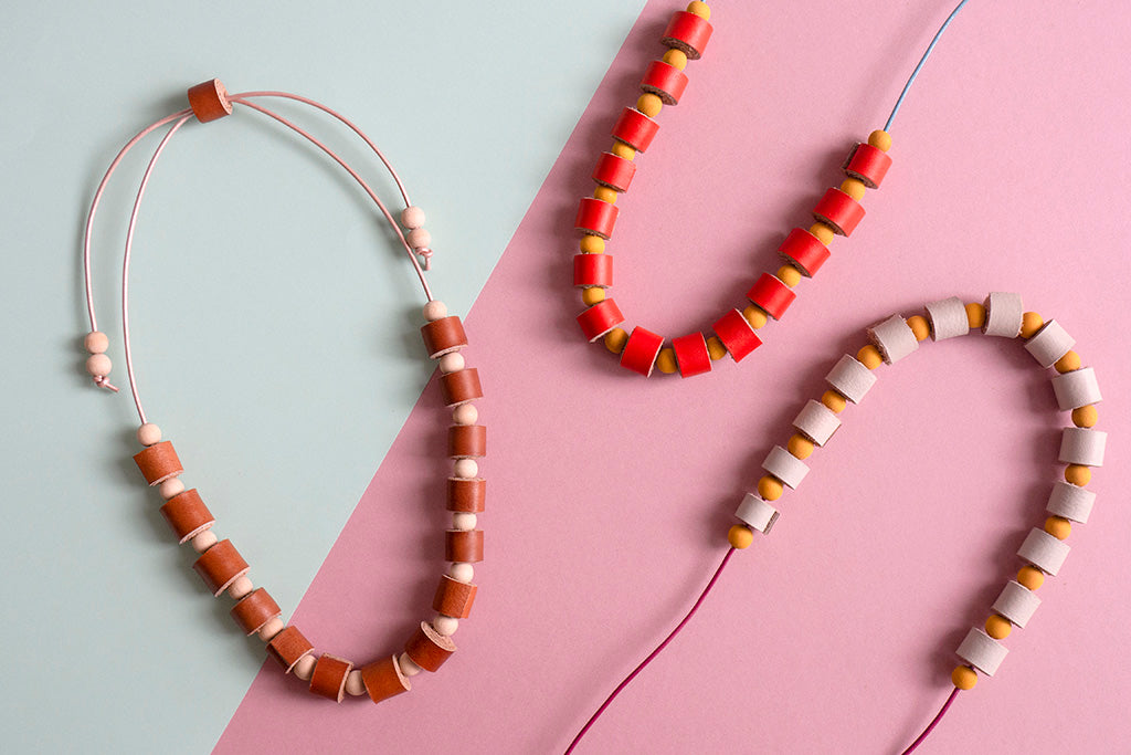 Las tres versiones de color de los collares, miel, naranja y vainilla sobre fondo de color rosado y celeste claro