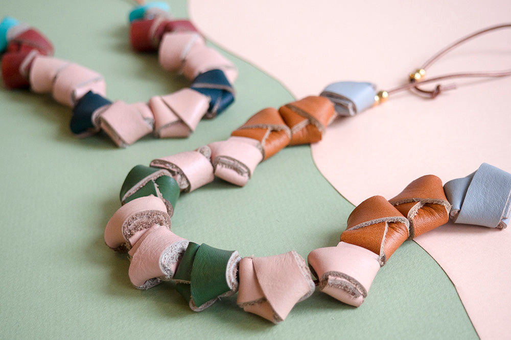 Detalle de cerca de los nudos de cuero en colores salmón, verde olivo, miel y gris sobre fondo de color verde y rosado